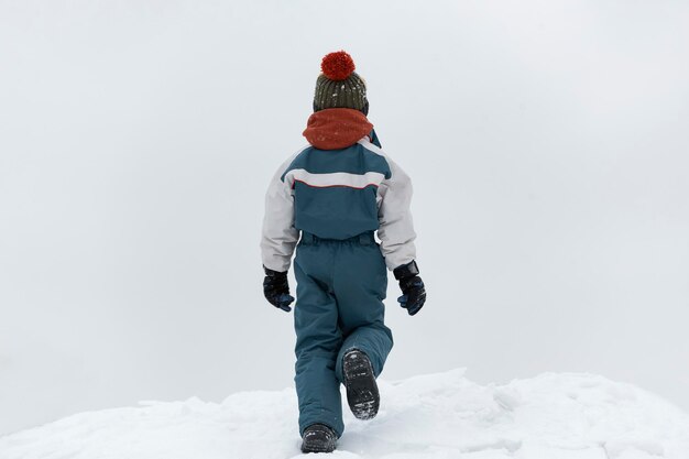 Rückansicht geht das Kind im Winter auf der Straße. Junge geht auf losem Schnee. Kalter Wintertag.