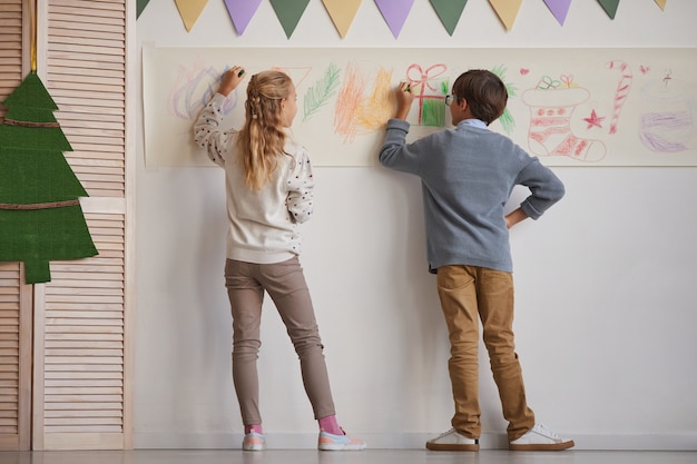 Rückansicht in voller Länge bei Jungen und Mädchen, die an Wänden zeichnen, während Kunstunterricht in der Schule genießen, Raum kopieren