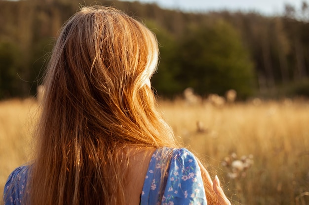 Rückansicht Nahaufnahme einer Ingwerfrau in blauem Sommerkleid mit Blumen, die frische Luft gegen die Sonne genießt