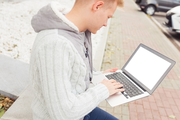 Rückansicht Nahaufnahme eines gutaussehenden jungen Mannes, der am Laptop arbeitet und auf der Stadtstraße lächelt, Kopierraum