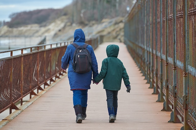 Rückansicht von Mutter und Sohn, die am Kai in der Nähe des Wintermeeres spazieren gehen?