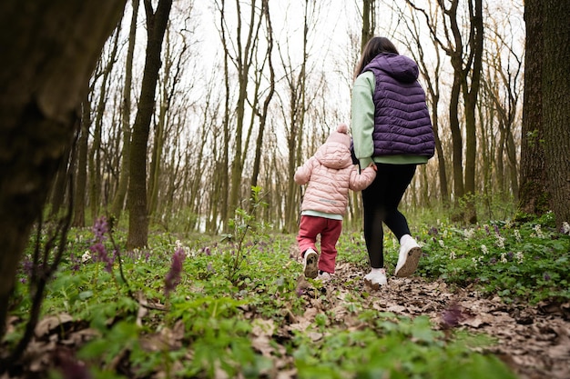 Rückansicht von Mutter und Tochter beim Spaziergang auf einem Waldweg. Frühlingsfreizeitkonzept im Freien