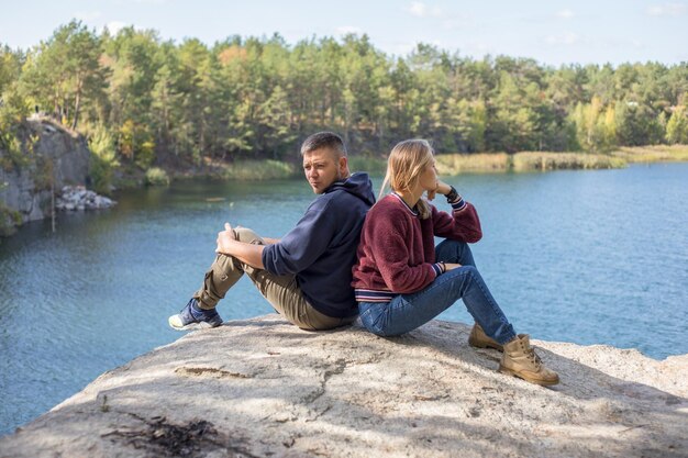 Rückansicht von netten, lieben Ehepartnern Verbringen Sie freie Freizeit im blauen See, sitzend auf Stein, die Sonne scheint