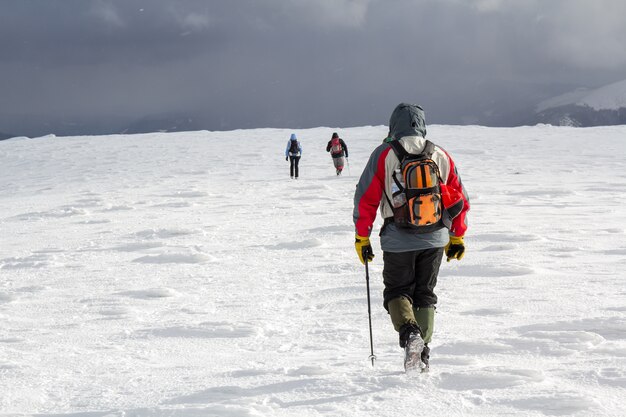 Rückansicht von Wanderern, die auf schneebedecktem Hügel in den Winterbergen gehen.