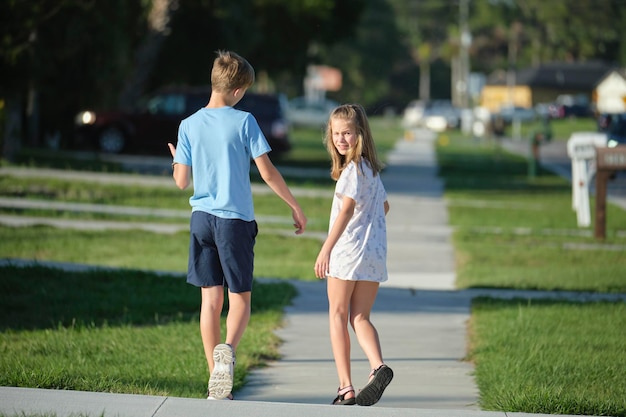 Rückansicht von zwei jungen Teenagern, Mädchen und Jungen, Bruder und Schwester, die an einem sonnigen Tag gemeinsam auf der ländlichen Straße spazieren Urlaubszeitkonzept