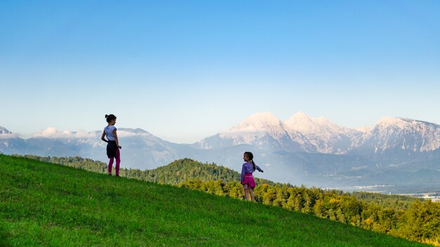 Rückansicht von zwei Kindermädchen, die auf einer Bergwiese stehen, jüngeres, das auf das Tal unten zeigt