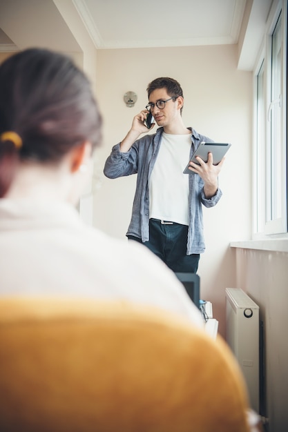 Rückansichtfoto einer kaukasischen frau, die in einem stuhl sitzt, während ihr geschäftspartner am telefon mit einem tablett in der hand spricht