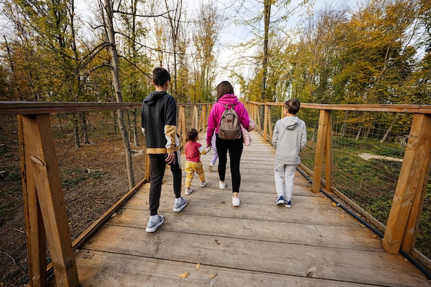 Rücken einer Mutter mit vier Kindern, die an einer Holzbrücke im Herbstwald spazieren geht