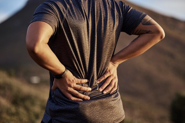 Rückenschmerzen beim Laufen und Verletzungen bei einem Mann in der Natur zum Fitnesswandern oder Training. Notfallunfall und Körperschmerzen mit Nahaufnahme eines männlichen Läufers im Freien wegen Muskelentzündung, Verspannungen oder Druck