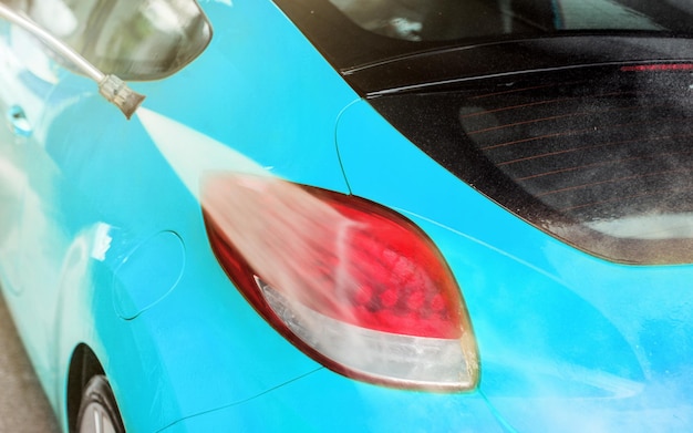 Rücklicht des blauen Autos, das in der Selbstbedienungswaschanlage gewaschen wurde, Wasser, das auf die rote Oberfläche sprüht.