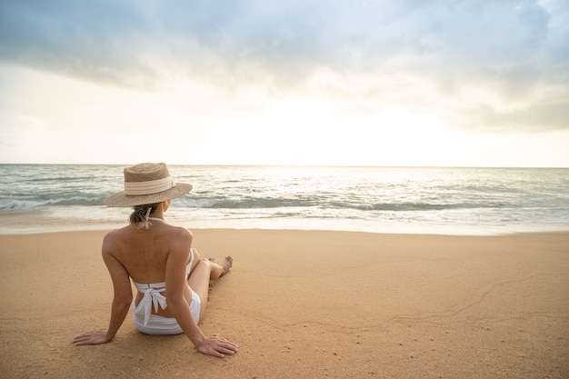 Rückseite der Frau im Bikini sitzt am Sandstrand entspannendes Sonnenbaden.