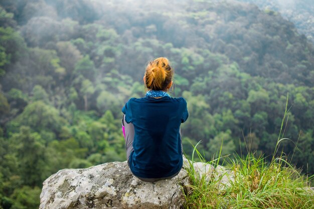 Rückseite der glücklichen Frau sitzend auf Felsen am Berg, der Ansicht mit Nebel schaut