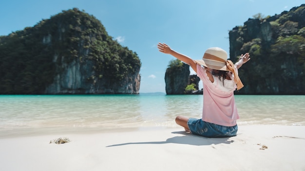 Rückseite des asiatischen Kindermädchens, das Hut trägt, der am Strand sitzt.