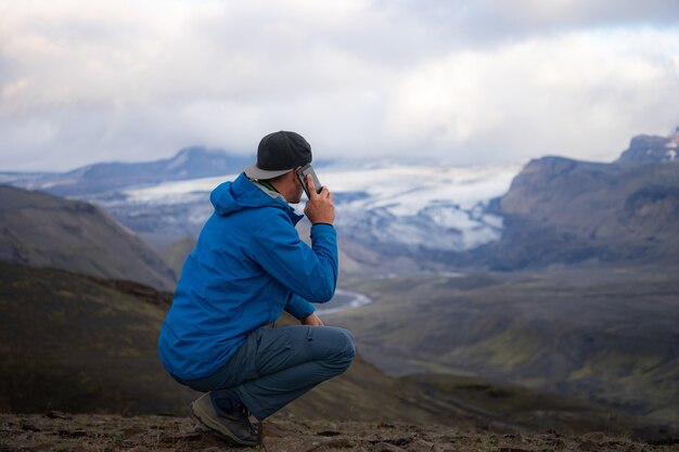 Rückseite des großen kaukasischen Mannes, der durch Handy nahe über Berg der Laugavegur-Spur in Island anruft.