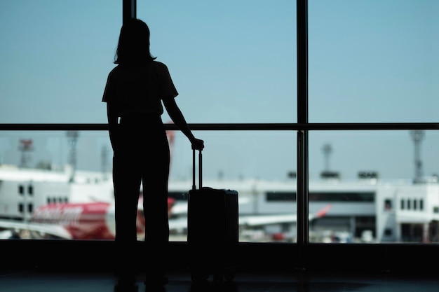 Rückwärtssicht Silhouette Frau steht mit Gepäck am Fenster im Flughafen