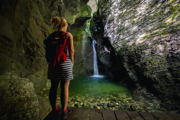 Rückwand einer Frau, die auf einem Bodenbrett gegen einen Wasserfall inmitten einer Felsformation steht