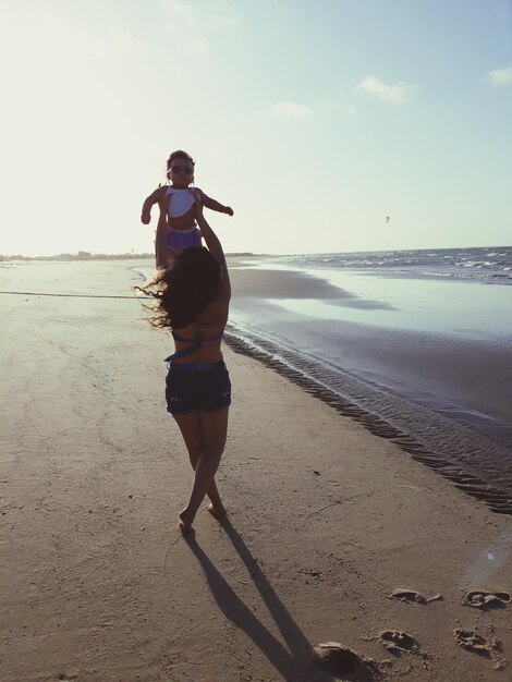 Foto rückwand einer frau, die mit ihrer tochter spielt, während sie am strand steht