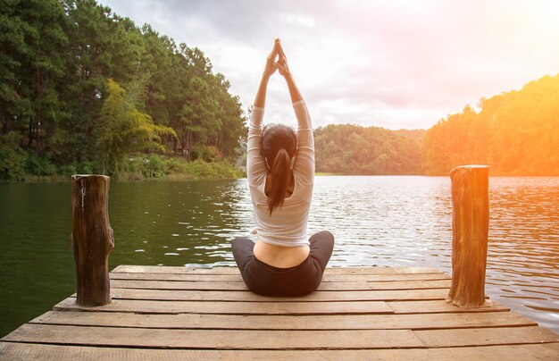 Foto rückwand einer frau, die yoga am pier über dem see gegen bäume übt