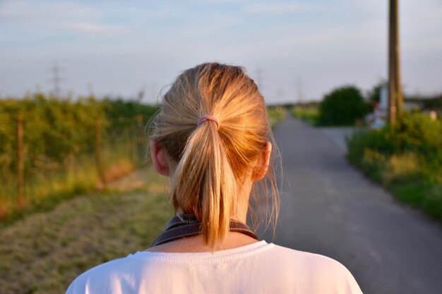 Foto rückwand einer frau mit pferdeschwanz, die auf der straße gegen den himmel steht