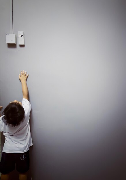 Foto rückwand eines jungen, der auf grauem hintergrund in richtung der sicherungskiste reicht