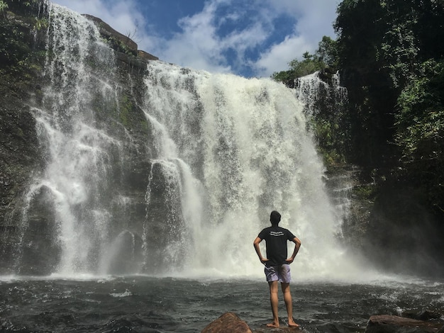 Rückwand eines Mannes mit Händen auf der Hüfte, der auf einen Wasserfall schaut