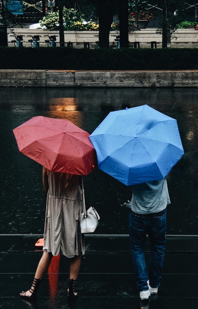 Foto rückwand eines mannes und einer frau mit einem regenschirm, die während der regenzeit auf der straße stehen