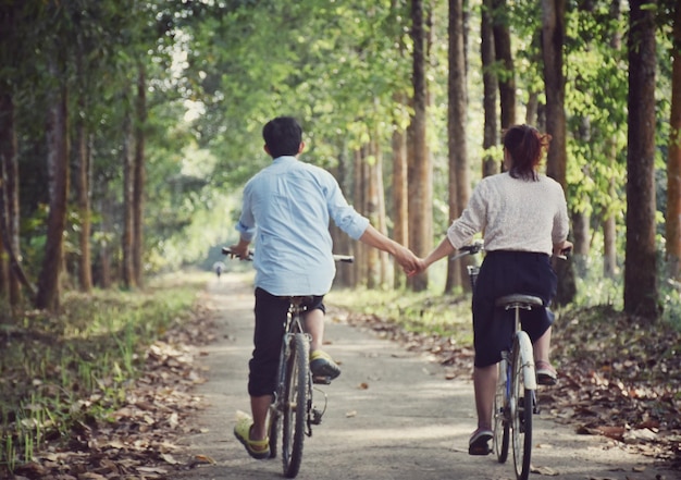 Rückwand eines Paares, das sich bei einem Fahrradfahrer inmitten von Bäumen an den Händen hält