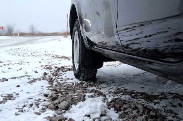 Rueda de coche con neumático de invierno en el camino de ripio en invierno