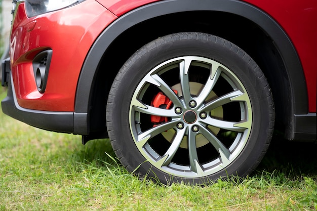 La rueda delantera de un coche rojo, que está aparcado en el césped.