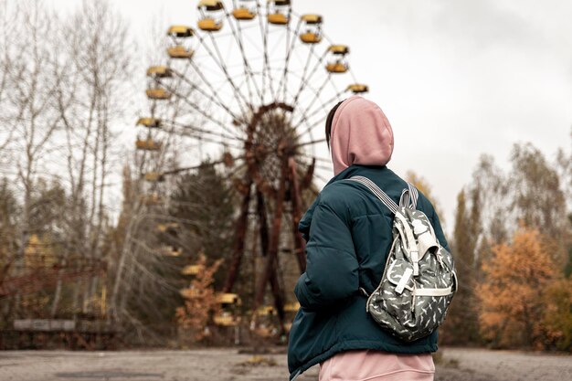 Rueda de la fortuna y turista chica con mochila en la ciudad de pripyat. Foto a través de alambre de púas oxidado. Zona de exclusión de 30 km de Chernóbil. día gris sombrío de otoño, clima depresivo y diversión abandonada