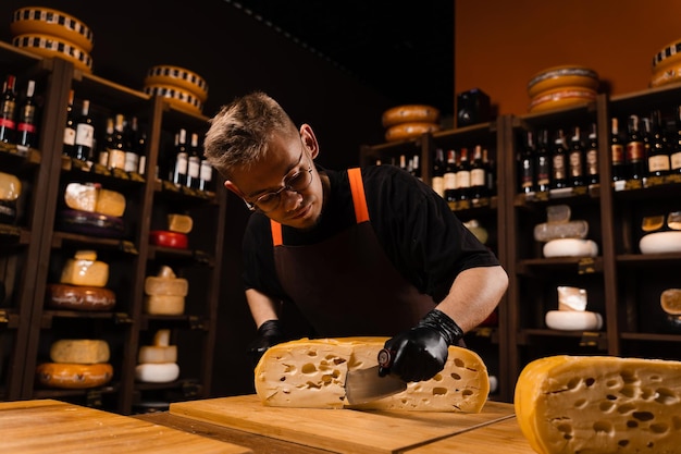 Rueda de queso maasdam limitada cortando queso en la tienda El sommelier de queso corta la rueda de queso amarillo cortada por la mitad con un cuchillo sobre la mesa