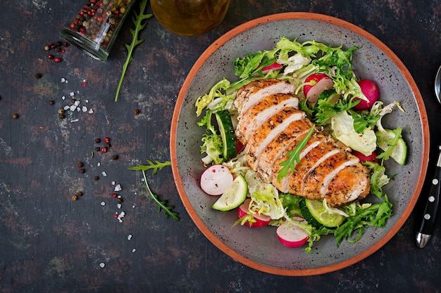 Ruede con la ensalada de verduras frescas y la pechuga de pollo cocida en un fondo oscuro.