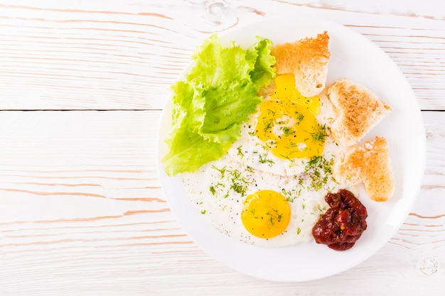 Rührei, gebratenes Brot, Ketchup und Salatblätter auf einem Teller auf dem Tisch