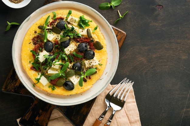 Rührei Leicht flauschig und butterig Rührei mit Feta-Käse, sonnengetrockneten Tomaten und schwarzen Oliven auf dem Teller über altem, dunklem, rustikalem Hintergrund aus Holz Leckeres Frühstück Draufsicht flach gelegt