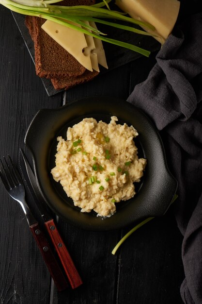 Rührei mit Frühlingszwiebeln serviert in dunkler Platte mit Brot auf dem Tisch