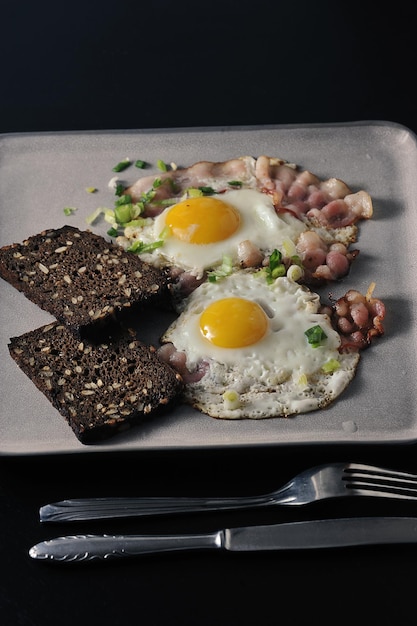 Rührei mit ganzen Eigelb, Speck, Frühlingszwiebeln und geröstetem Brot mit Körnern