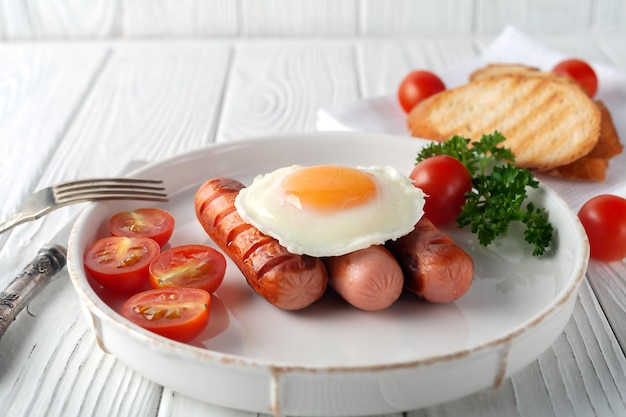 Rührei mit Würstchen, Tomaten und Toast auf weißem Holzhintergrund