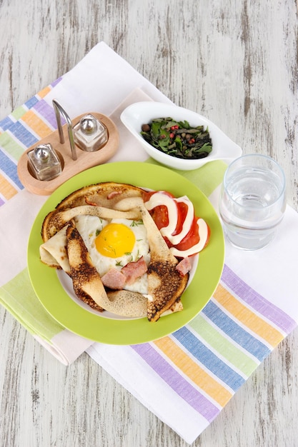 Rührei und Pfannkuchen auf Teller auf Serviette auf Holztisch