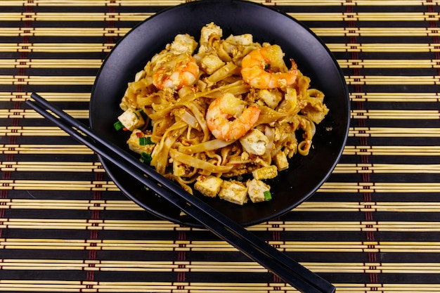 Foto rühren sie gebratene reisnudeln pad thai mit garnelen und tofu in der platte auf bambusmatte draufsicht thailändisches essen