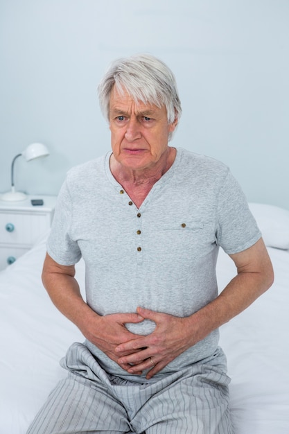 Rührender Magen des älteren Mannes beim Sitzen auf Bett