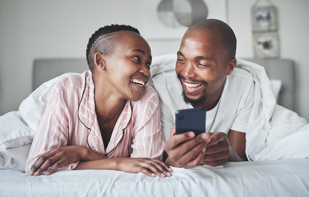 Rufen Sie soziale Medien an und morgens mit einem schwarzen Paar im Schlafzimmer, um sich auf einem Bett in ihrem Zuhause zu entspannen. Mobiles Meme oder Kontakt mit einem Mann und einer Frau, die im Internet surfen, sich entspannen oder verbinden