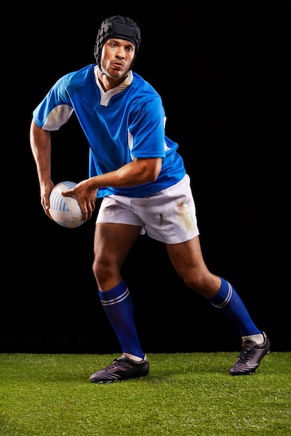 Rugby escuro e homem atleta esportivo passa uma bola à noite em fundo de estúdio preto treinando bem-estar e fitness Treino de exercícios e carreira profissional de esporte masculino ou jogador na grama