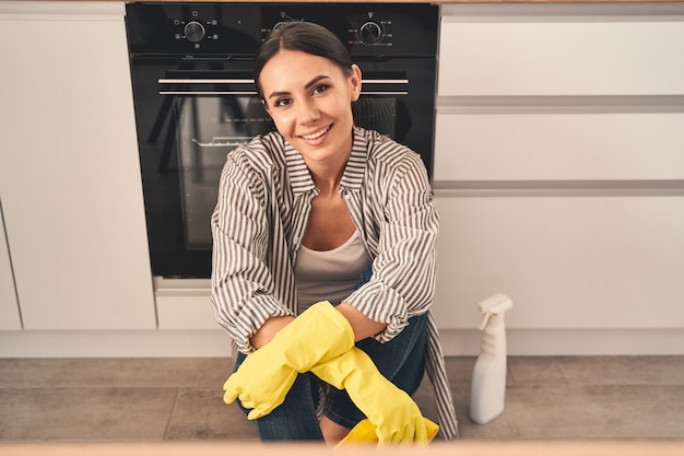 Ruhen Sie sich aus. Begeistertes brünettes Mädchen, das Positivität ausdrückt, während es sich nach der Reinigung ihrer Wohnung ausruht