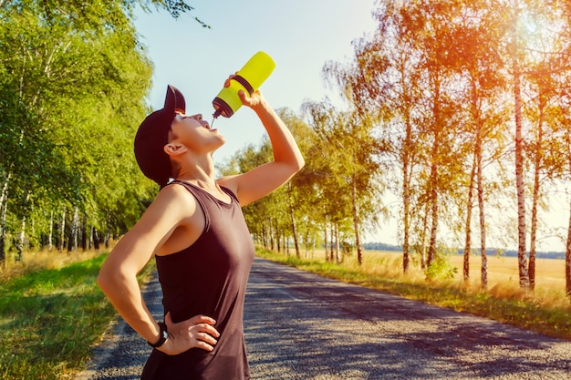 Ruhende junge Frau trinkt Wasser aus Plastikflasche nach hartem Training