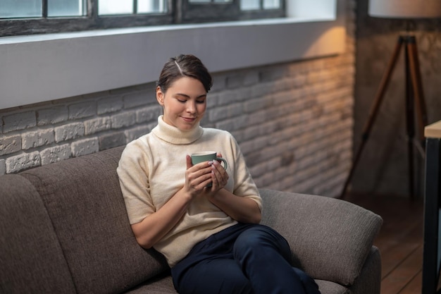 Ruhige Dame mit einem Getränk, das auf dem Sofa sitzt