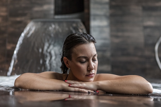 Ruhige Frau, die im Pool mit Wasserstrom sich entspannt