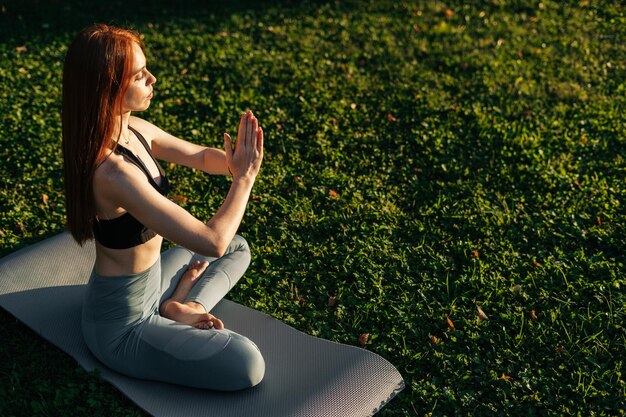 Ruhige junge Dame mit geschlossenen Augen meditiert in Lotusposition auf einer Yogamatte
