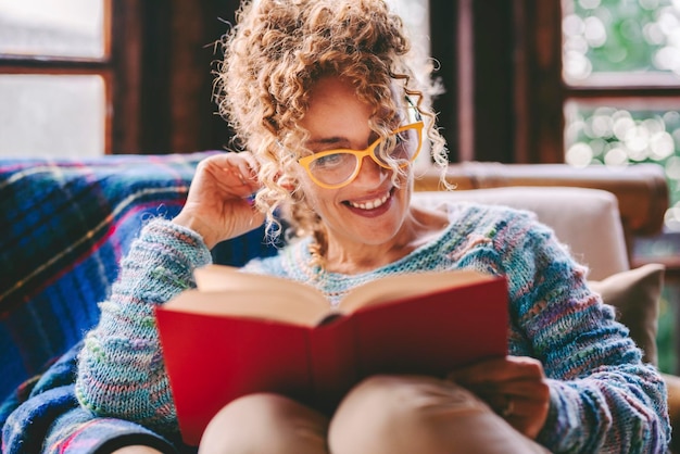 Ruhige Menschen, die sich entspannen und Indoor-Freizeitaktivitäten zu Hause genießen, ein Buch mit rotem Einband lesen Bildung Konzept Lifestyle Ein glückliches weibliches Volk liest einen Roman, der zu Hause sitzt Lächelnde Dame genießt