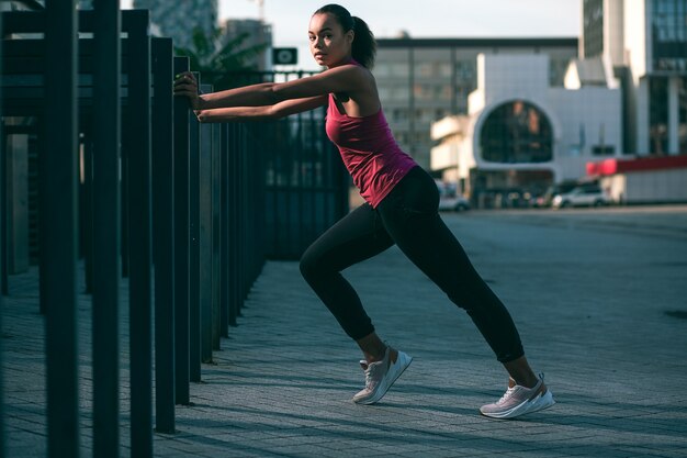 Ruhige schlanke Sportlerin, die Hände auf das Geländer legt und es in ihrem Training verwendet