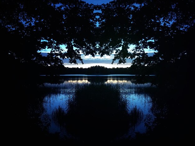 Ruhige Seeoberfläche am Abend in Lettland, Osteuropa. Sommersonnenunterganglandschaft mit Wasser und Wald.